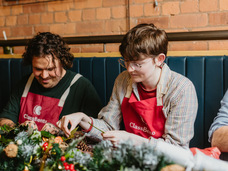 Two smiling people making Christmas wreaths